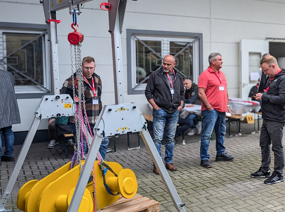 Männer, die ein großes, gelbes Bauteil, das von einer Traverse gehalten wird, begutachten