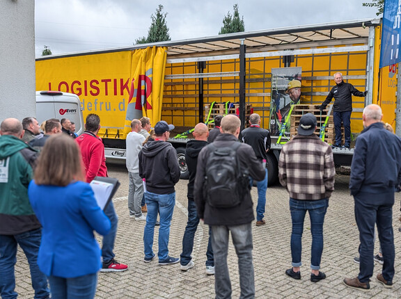 Eine Gruppe an Menschen beobachten eine Vorführung am offenen LKW-Anhänger.